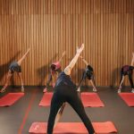 Yoga class with diverse adults stretching on mats in a cozy wooden studio.